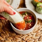 hand dipping a tofu spring roll into the peanut sauce; side angled view.
