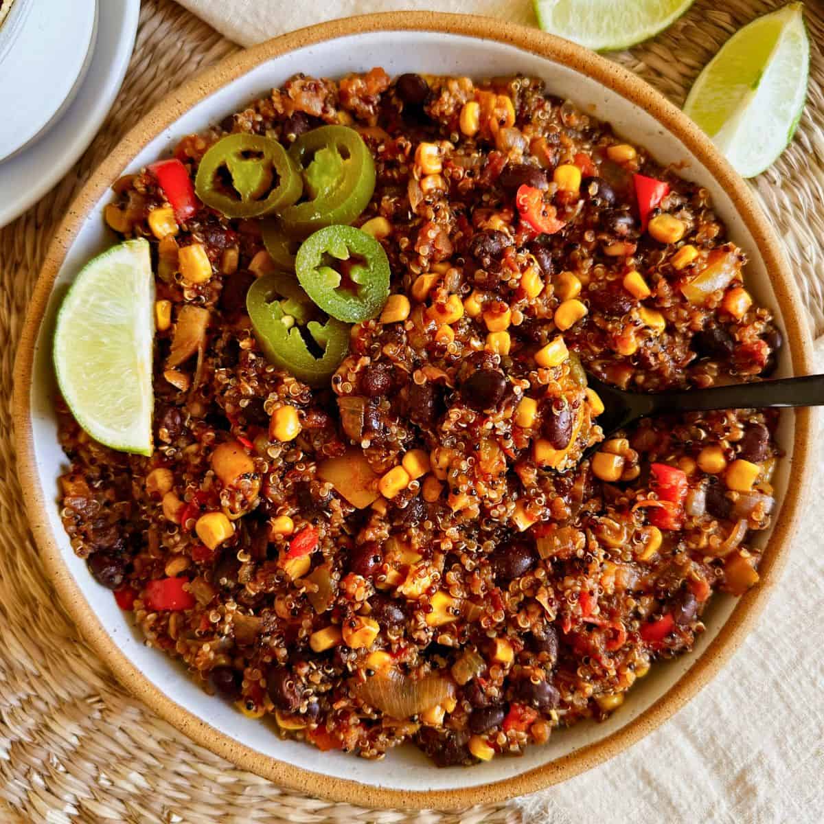 Top view of black bean quinoa chili in a bowl with a spoon hanging in it and topped with jalapenos and a lime wedge.