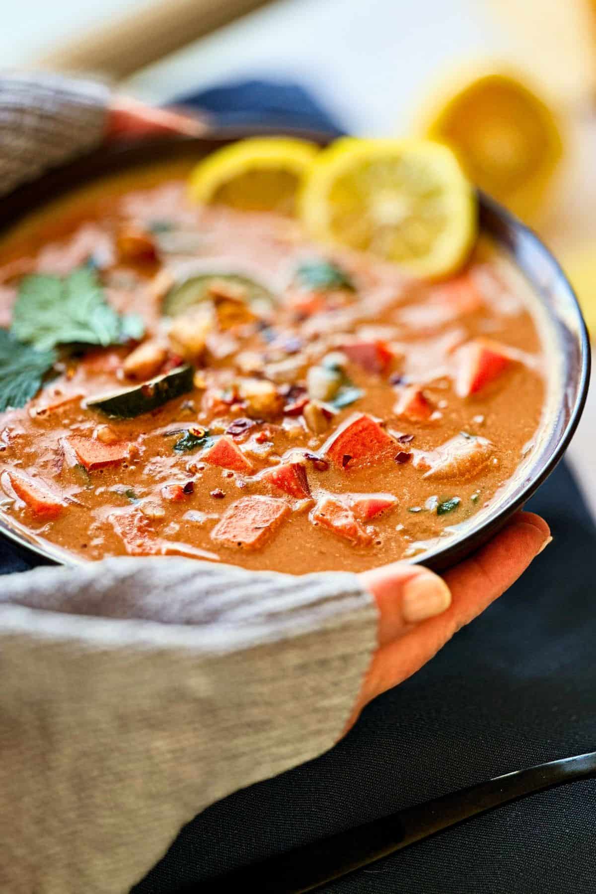 hands holding a bowl of the stew from a side view.