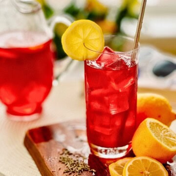 glass of blueberry lavender lemonade with a straw and a slice of lemon.