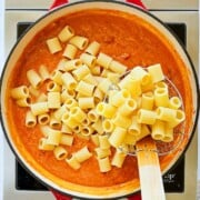 adding pasta to a pan of vegan vodka sauce.