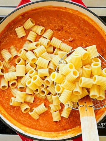 adding pasta to a pan of vegan vodka sauce.