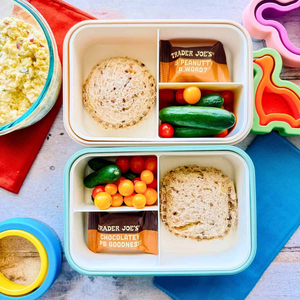 two bento boxes containing the eggless salad pockets, mini tomatoes, cucumbers, and peanut bar.