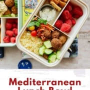 Overhead view of a colorful Mediterranean lunch bowl in a bento-style container with couscous, mini falafel, cucumber, shredded carrots, cherry tomatoes, spinach, raspberries, pita chips, and a small container of vegan tzatziki. Text overlay reads “Mediterranean Lunch Bowl – Perfect for Work or School Lunches.”