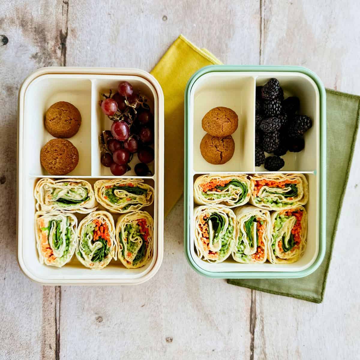 Two bento boxes with the hummus and veggie pinwheels, cookies, blackberries, and grapes.