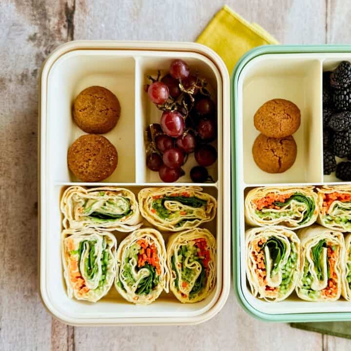 Two bento boxes with the hummus and veggie pinwheels, cookies, blackberries, and grapes.