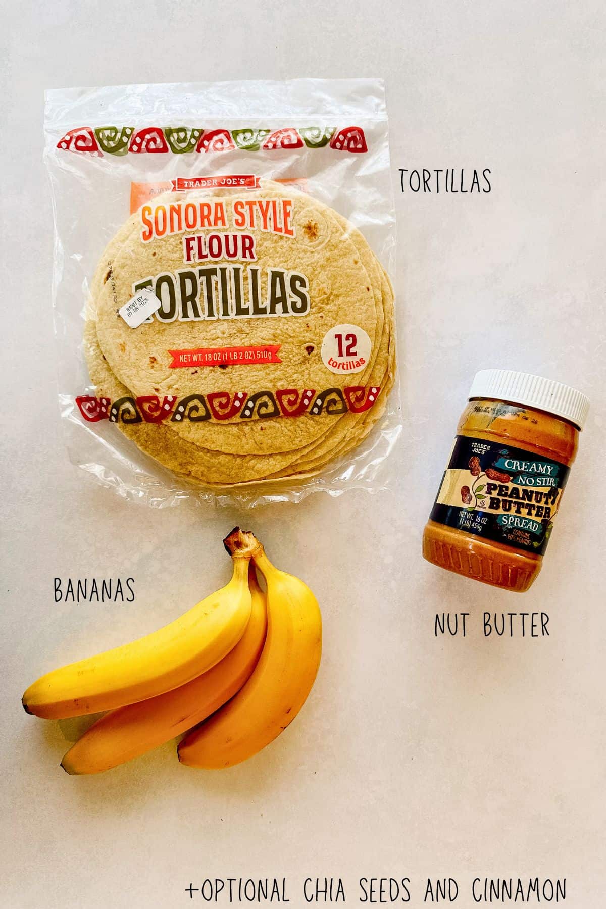 Flat lay of ingredients for peanut butter and banana roll-ups, including a package of Trader Joe’s Sonora Style Flour Tortillas, a bunch of bananas, and a jar of creamy no-stir peanut butter. Optional additions like chia seeds and cinnamon are noted in text.