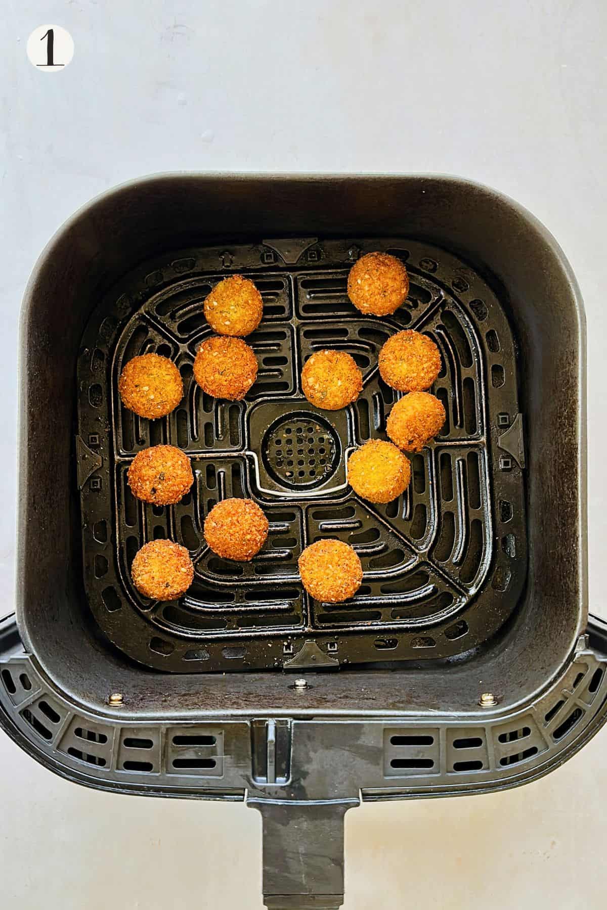 Mini falafel arranged in a single layer inside an air fryer basket, golden and crisp after cooking.