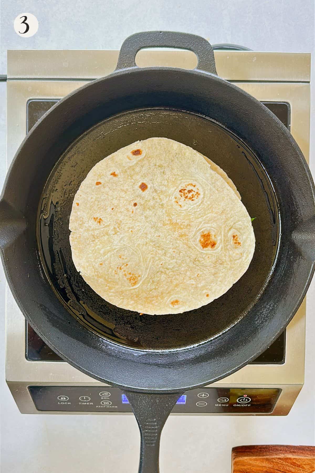 A quesadilla is being cooked on a cast iron skillet until golden brown on the bottom.