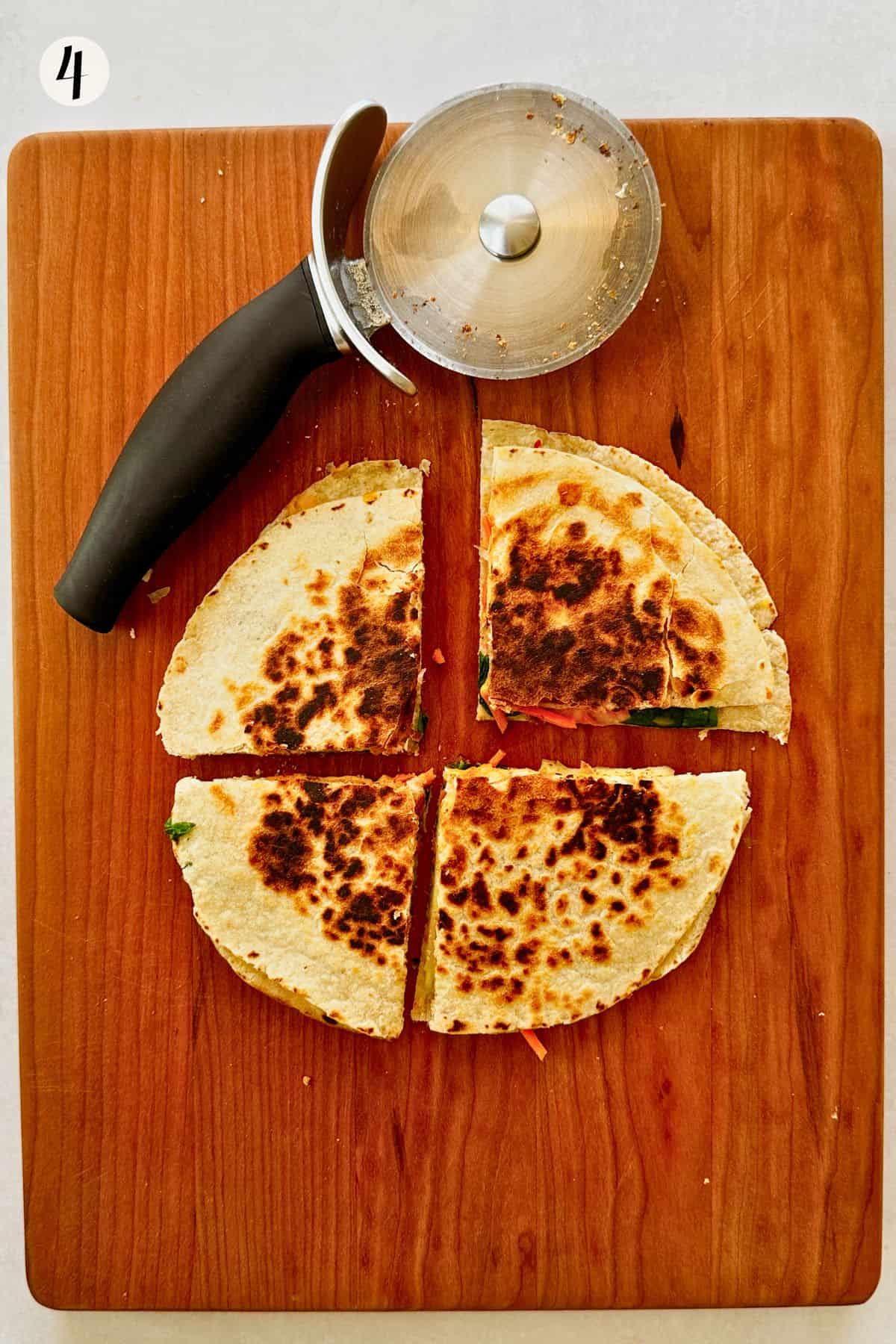 A cooked quesadilla cut into triangles with a pizza cutter on a wooden cutting board, ready to serve.