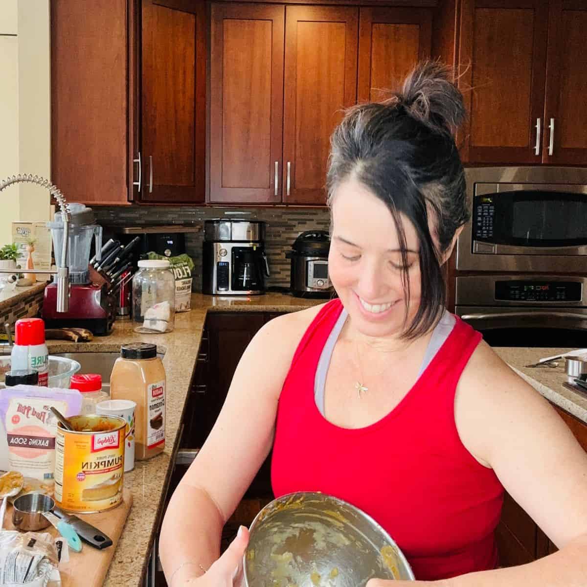 Reg smiling in a red tank top mixing ingredients in a large bowl in a home kitchen surrounded by baking supplies.