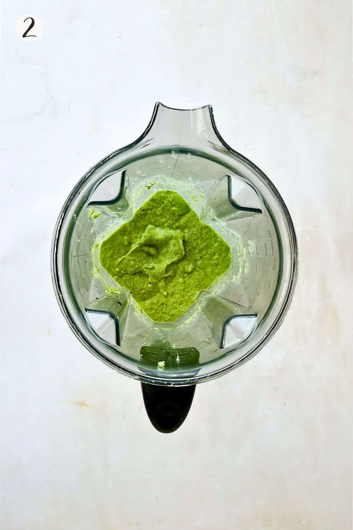 Top-down view of a blender filled with bright green cucumber gazpacho after blending the vegetables into a creamy soup.