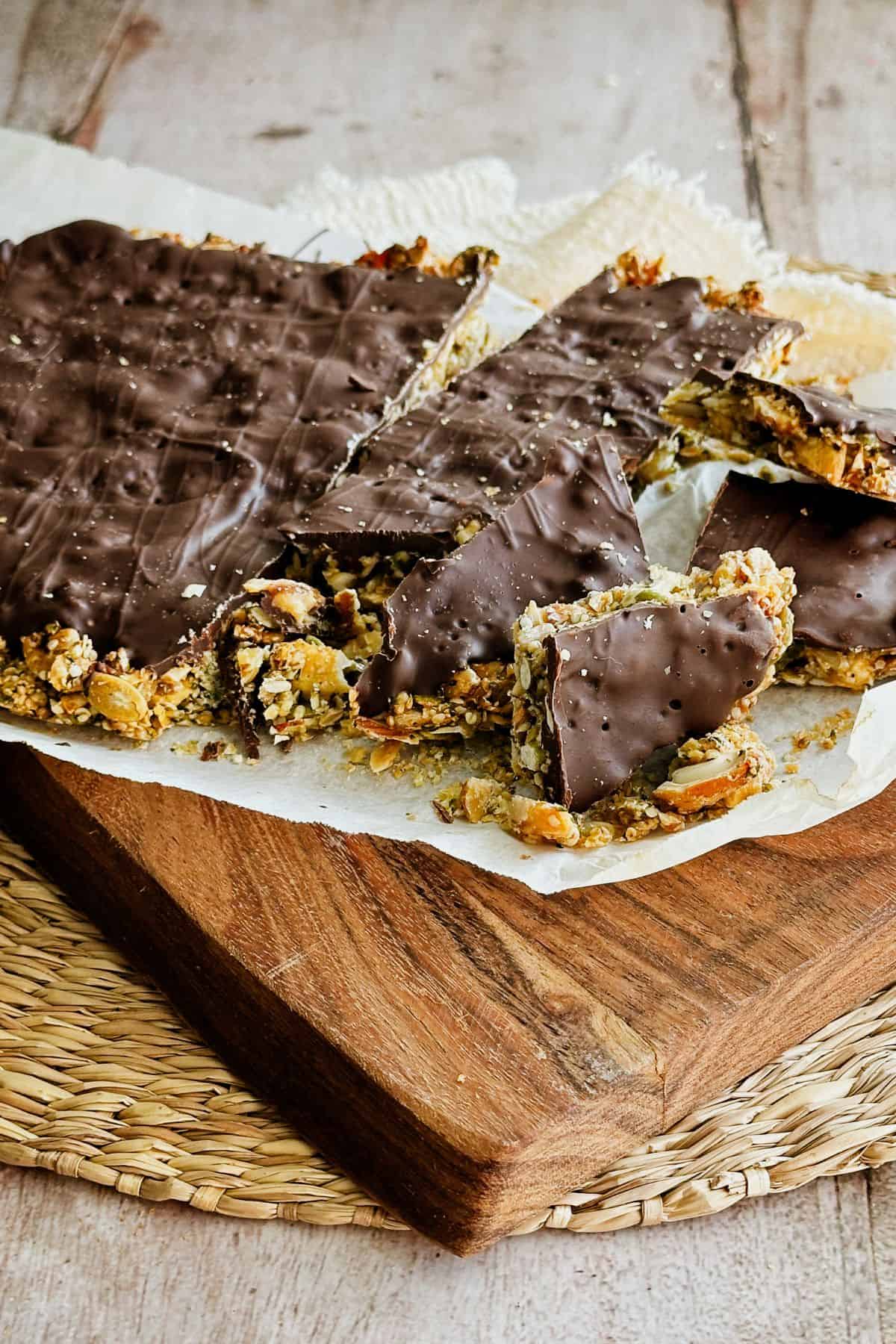 Homemade vegan chocolate bark with nuts and seeds, broken into rustic shards on parchment paper over a wooden board.