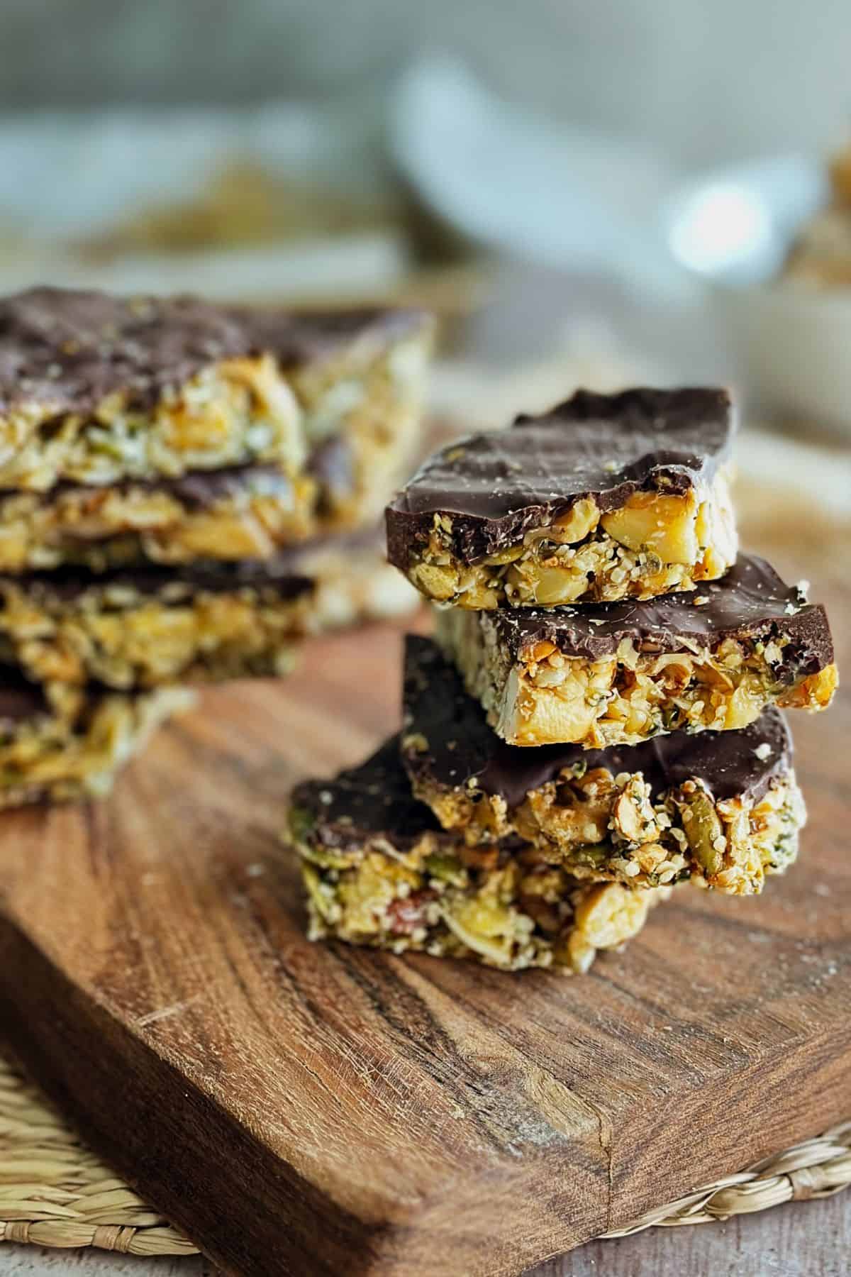 Stack of homemade vegan chocolate bark with nuts and seeds on a wooden board, showing the crunchy layers and rich chocolate coating.