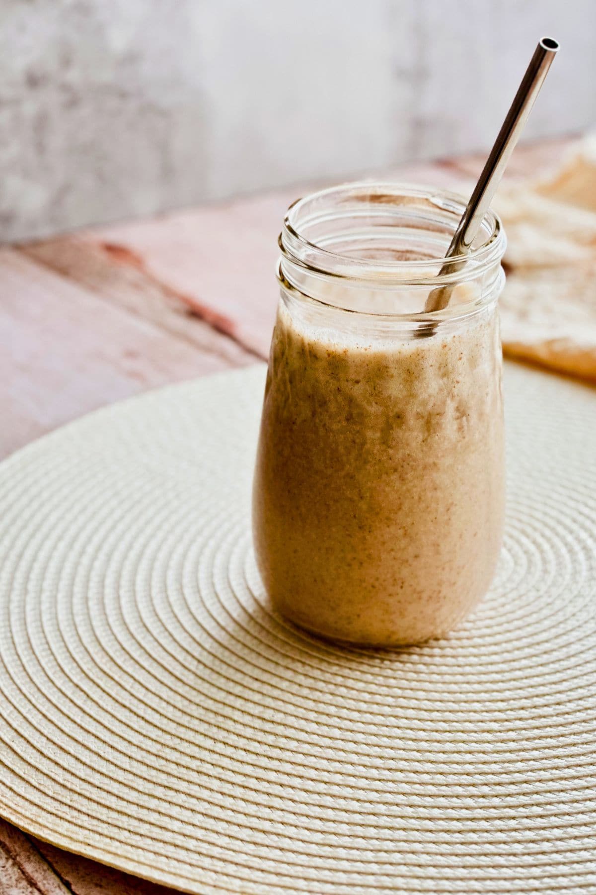  A glass jar filled with creamy batido de trigo (Cuban wheat milkshake) with a metal straw, set on a light woven placemat.