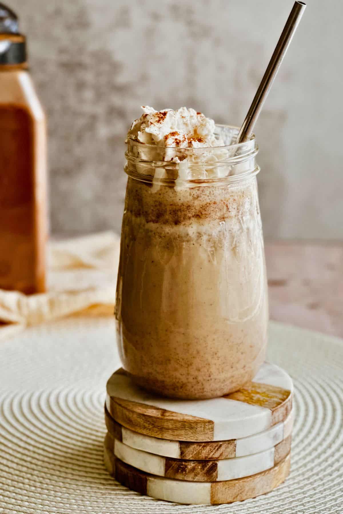 A mason jar of Cuban Batido de Trigo (wheat milkshake) topped with vegan whipped cream, cinnamon, and served with a metal straw.