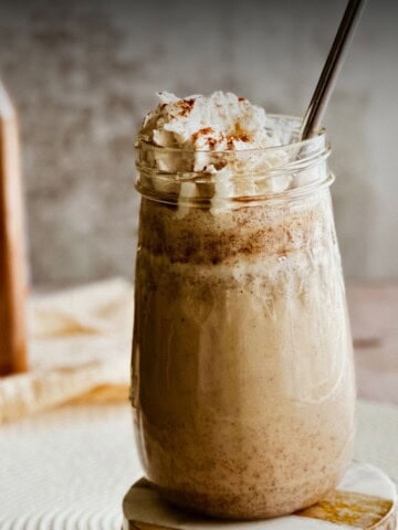 A tall glass of Cuban Batido de Trigo (wheat milkshake) topped with vegan whipped cream, cinnamon, and served with a metal straw.