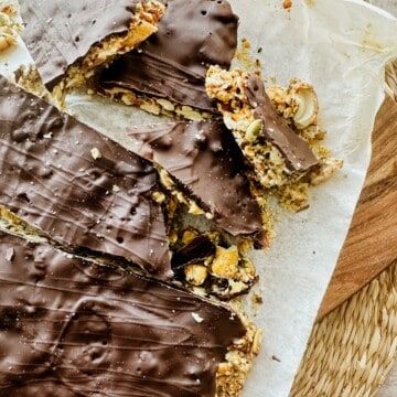 Overhead view of sliced vegan chocolate bark with nuts and seeds on parchment paper, highlighting the rustic shards and chocolate drizzle.