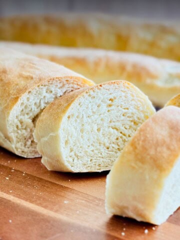 Close-up of sliced Cuban bread (pan Cubano) on a wooden cutting board, showing its fluffy, airy crumb and thin, golden crust
