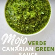Graphic with text reading ‘Mojo Verde Canarian Green Sauce – Great for Tapas!’ Close-up of a bowl filled with vibrant green mojo verde sauce, the texture slightly chunky and glossy.