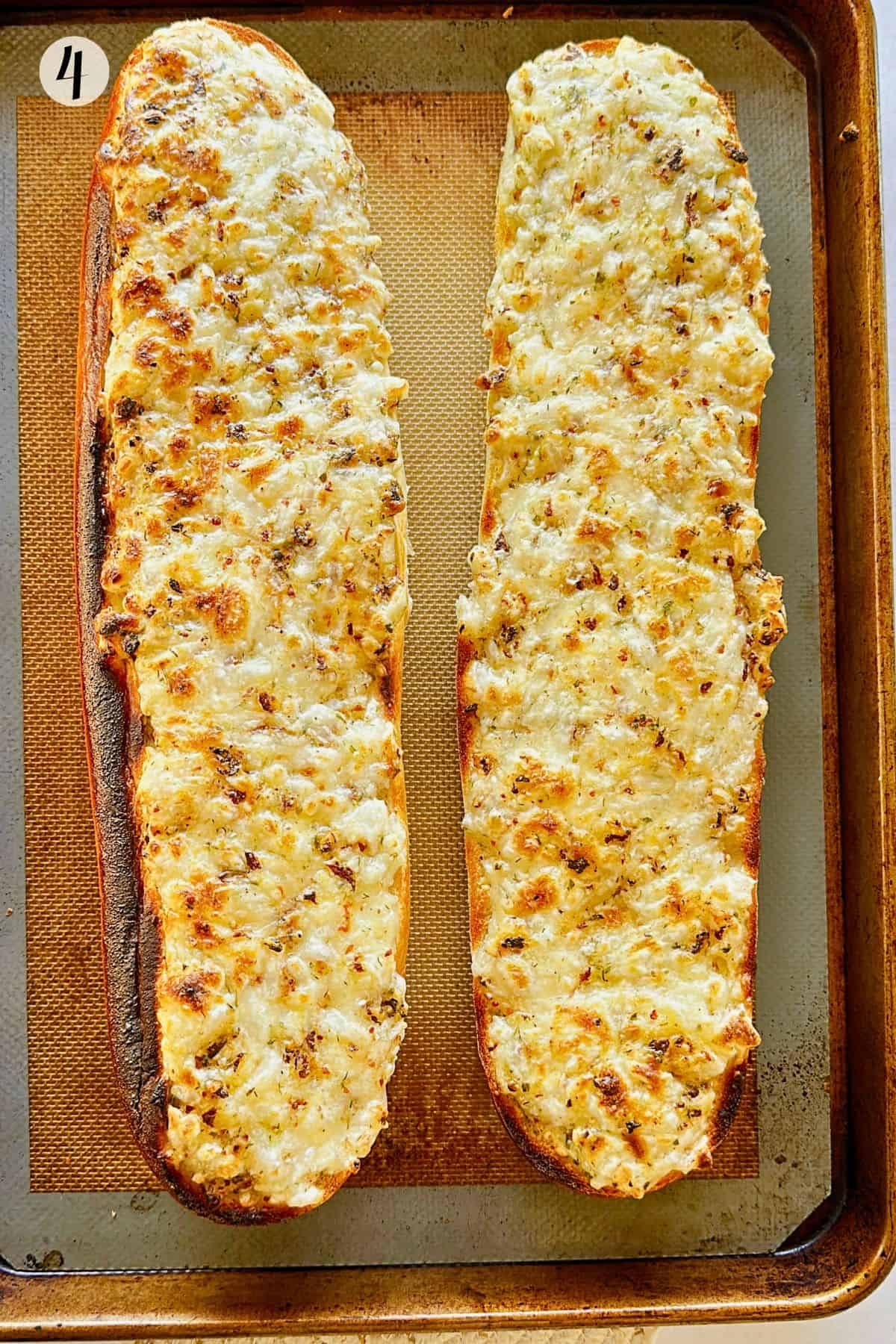 Two halves of French bread fresh from the oven on a baking sheet, topped with golden, bubbly melted vegan cheese and herbs.