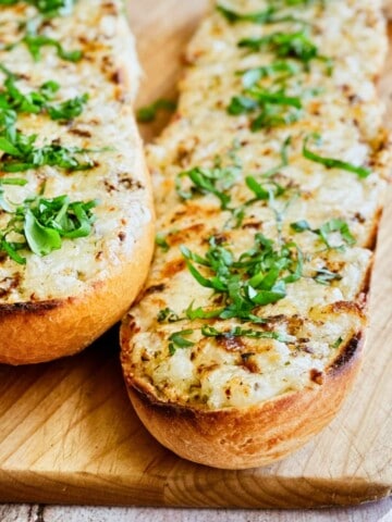 Golden toasted bread topped with melted vegan cheese and fresh basil, served on a wooden board.
