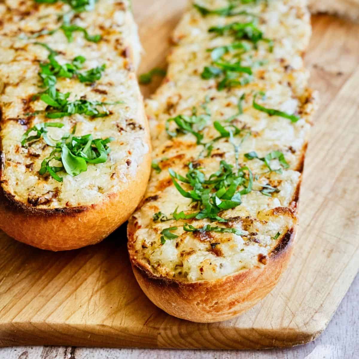 Golden toasted bread topped with melted vegan cheese and fresh basil, served on a wooden board.