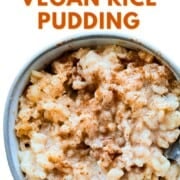 Overhead shot of a bowl filled with creamy vegan rice pudding topped with a sprinkle of cinnamon. The text overlay reads ‘How to Make Vegan Rice Pudding’ in bold letters. The pudding looks thick, glossy, and comforting with visible grains of rice coated in a sweet sauce.