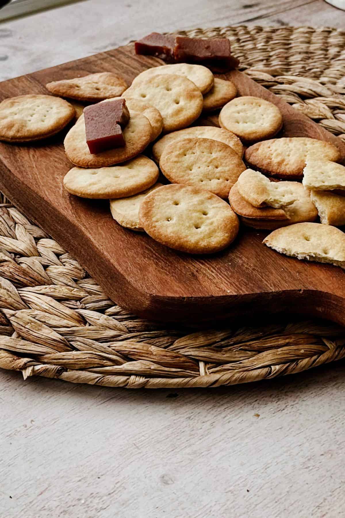 Golden Cuban crackers on a wooden board with a piece of guava paste on top, showing their crisp, flaky texture.