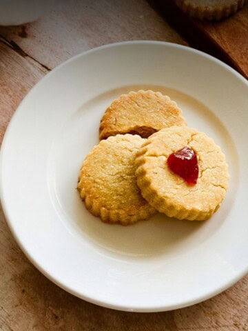 Three Cuban Shortbread Cookies (Torticas de Morón) on a white plate, one topped with a small piece of guava paste in the center.