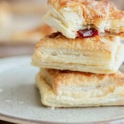 A stack of golden, flaky pastelitos de guayaba on a plate. The top one has a bite showing red guava filling. Text reads “Pastelitos de Guayaba.”