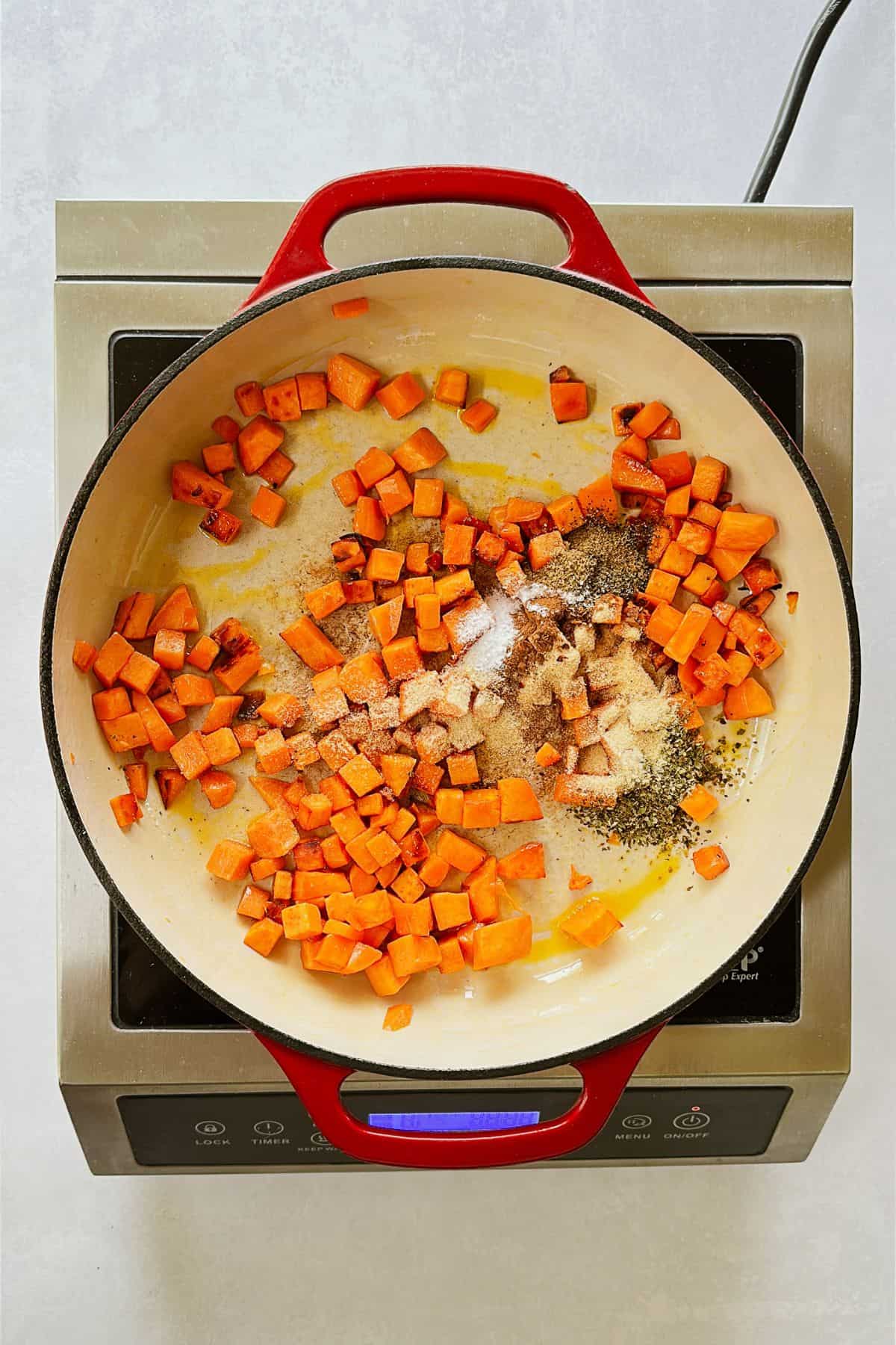 The red pot shows sweet potato cubes mixed with a colorful blend of spices - oregano, garlic powder, onion powder, and more - being stirred in to coat everything evenly.