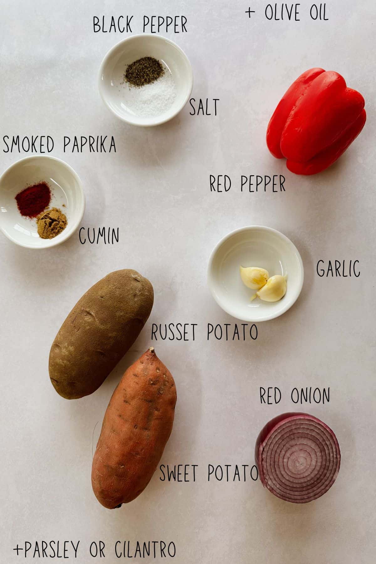 Overhead view of ingredients for sweet potato and russet hash, including potatoes, red onion, bell pepper, garlic, spices, and herbs, all labeled.