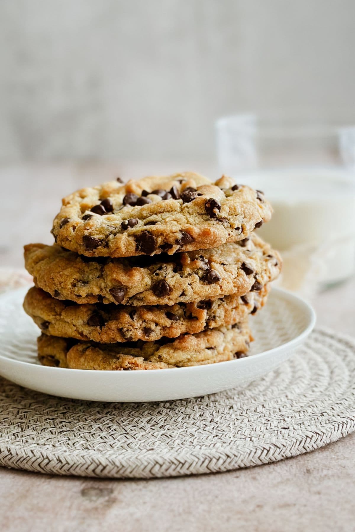 Stack of vegan chocolate chip cookies on a white plate. Glass of milk is in the back.