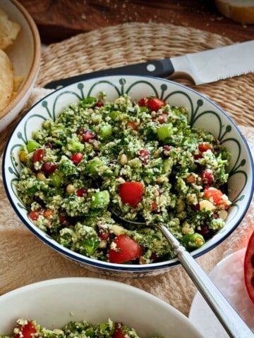 Overhead view of cauliflower tabbouleh in a bowl with fresh herbs, tomatoes, and pomegranate seeds, ready to serve.