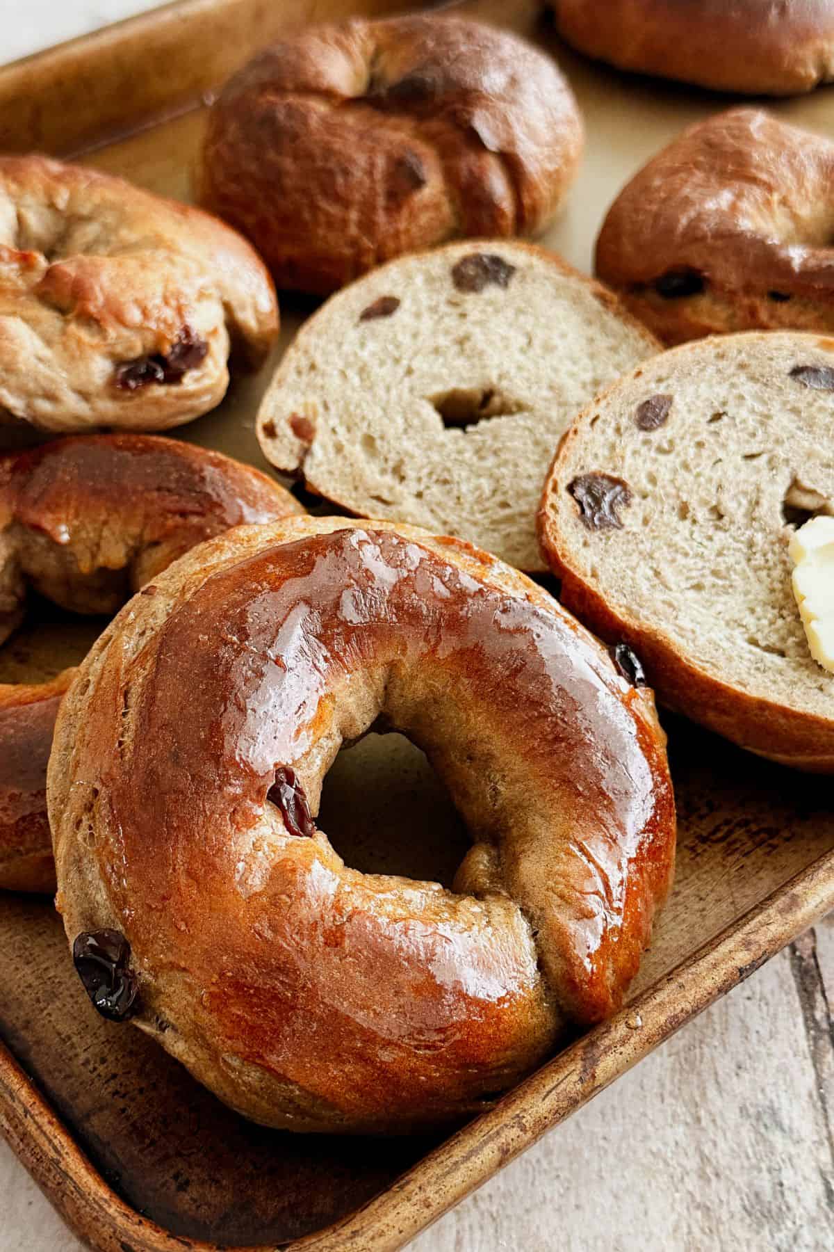 Freshly baked cinnamon raisin bagels with a glossy crust on a baking tray, with sliced bagels showing a soft crumb and raisins inside.