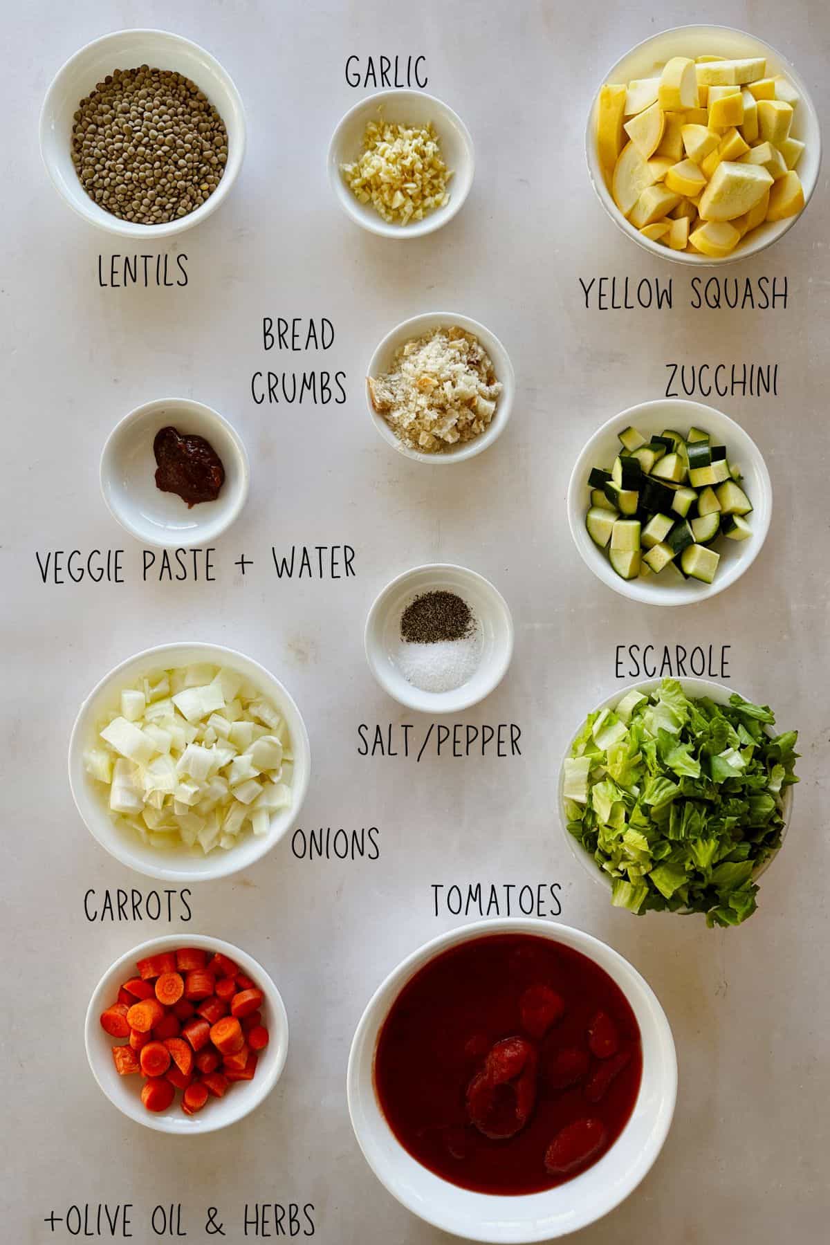 Bowls of lentils, chopped onion, carrots, zucchini, yellow squash, escarole, garlic, tomatoes, breadcrumbs, veggie paste, salt, pepper, and olive oil and herbs labeled.