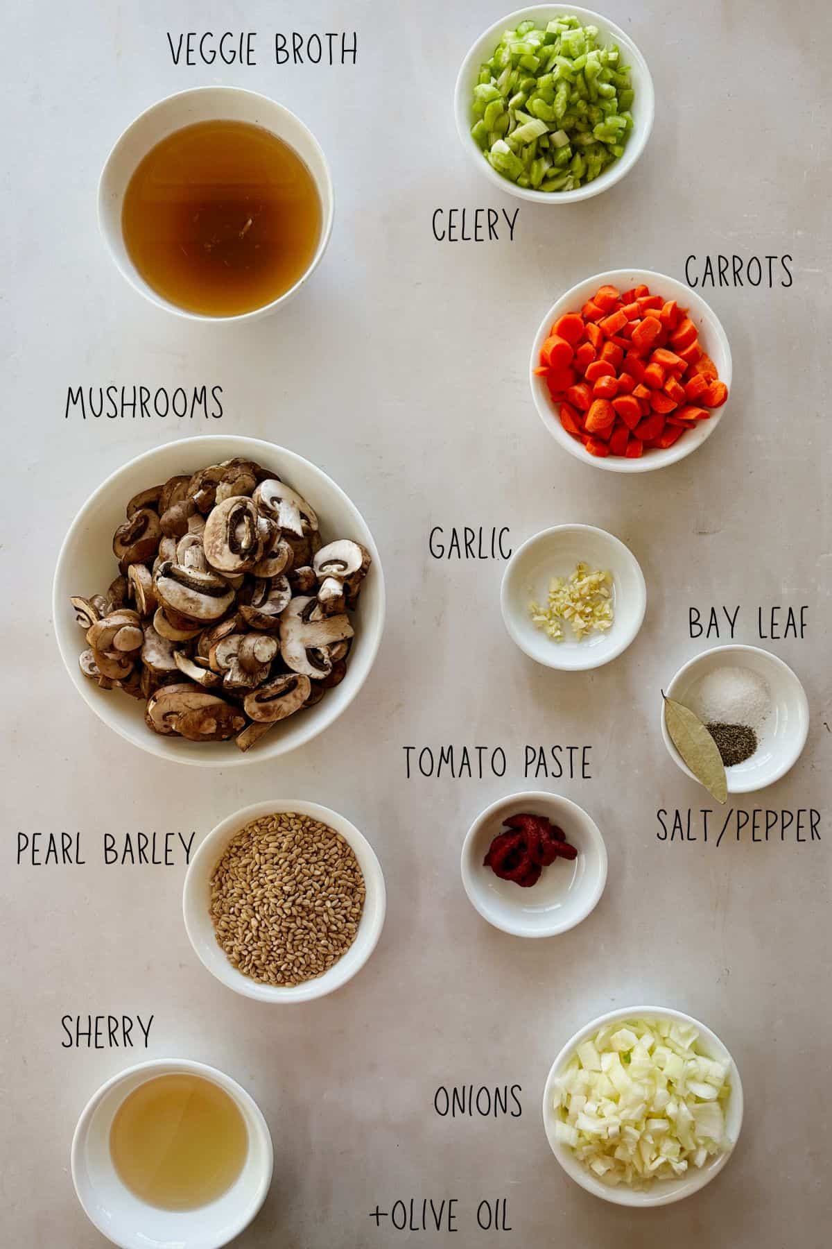 Overhead image of labeled ingredients for mushroom barley soup, including mushrooms, carrots, celery, pearl barley, garlic, onion, and broth.
