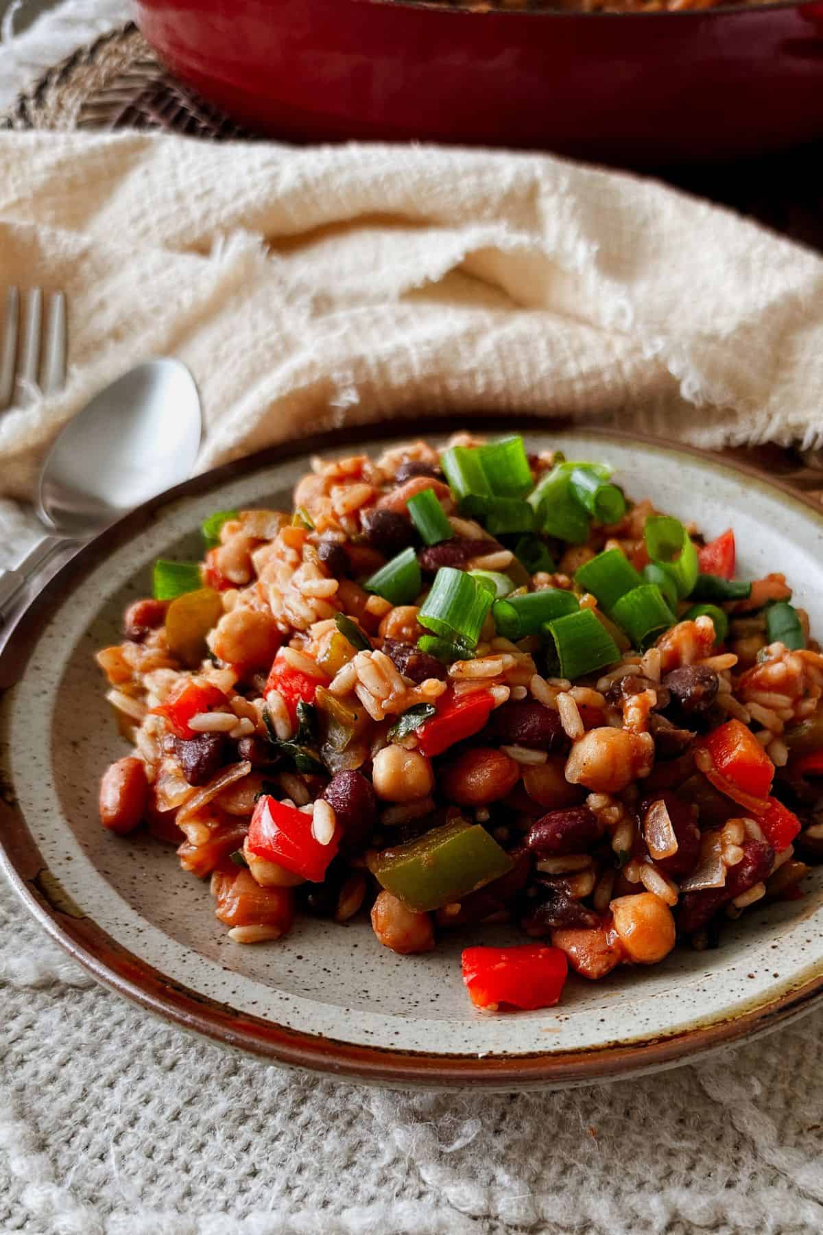 Close-up of skillet rice and beans with peppers and chickpeas, topped with chopped green onions on a ceramic plate.