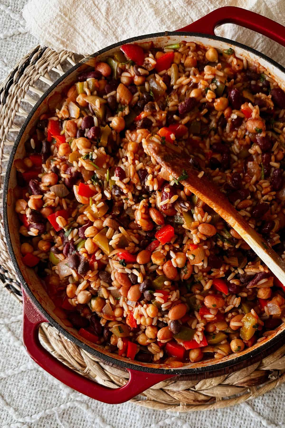 Top-down view of skillet rice and beans with peppers and onions in a red Dutch oven with a wooden spoon.