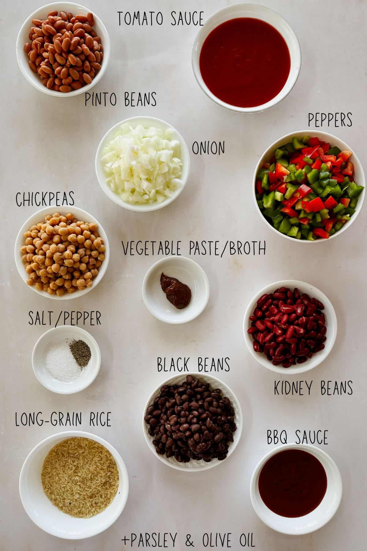 Labeled bowls of long-grain rice, pinto, black, kidney beans, chickpeas, chopped onion, peppers, tomato sauce, BBQ sauce, veggie paste, salt, pepper, parsley, olive oil.