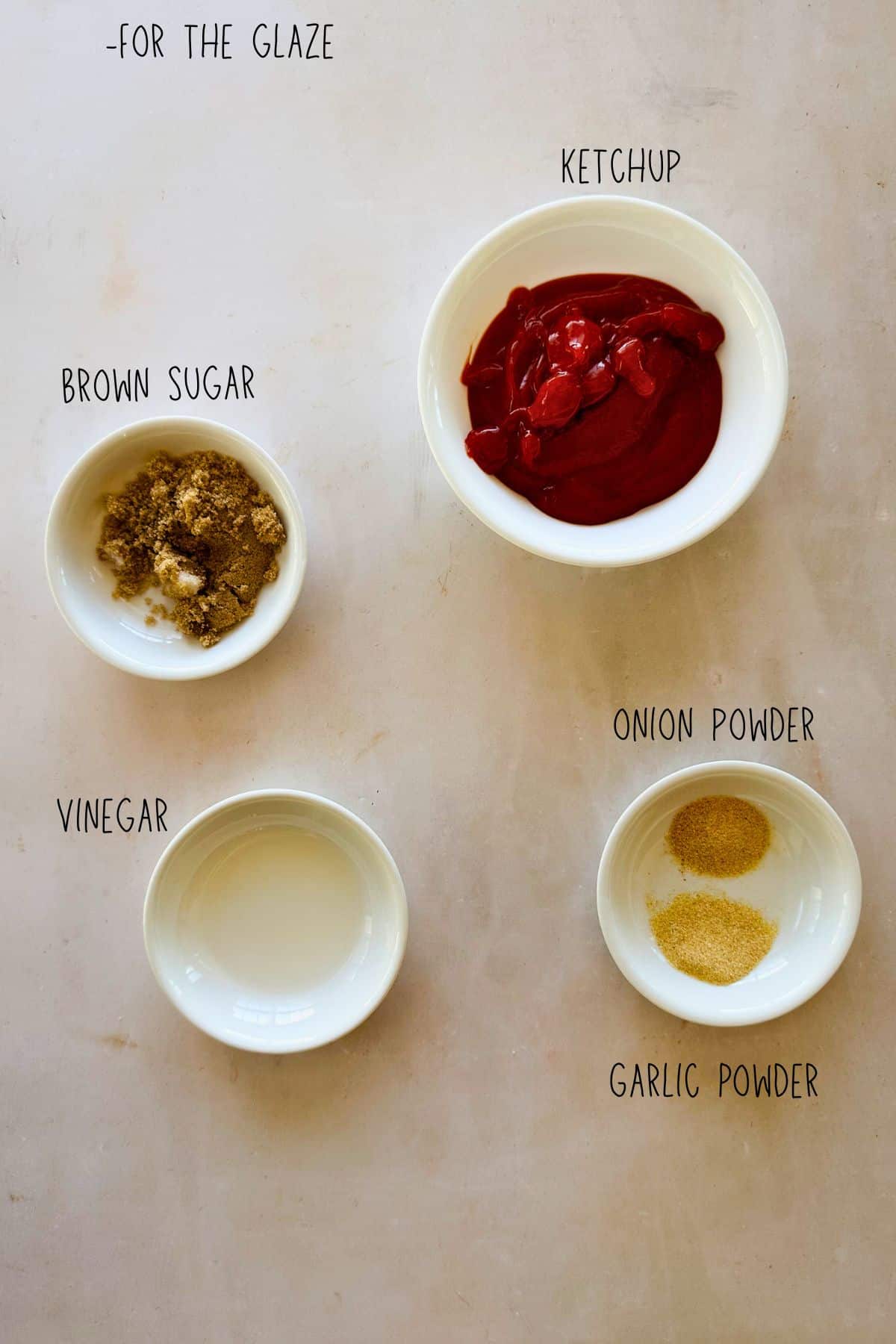 Small bowls of lentil loaf glaze ingredients arranged on a light surface, including ketchup, brown sugar, vinegar, garlic powder, and onion powder, labeled.