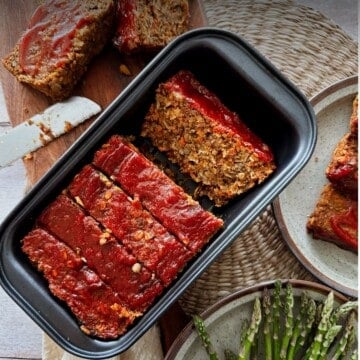 Sliced vegan lentil loaf in a black loaf pan, topped with a glossy ketchup glaze.