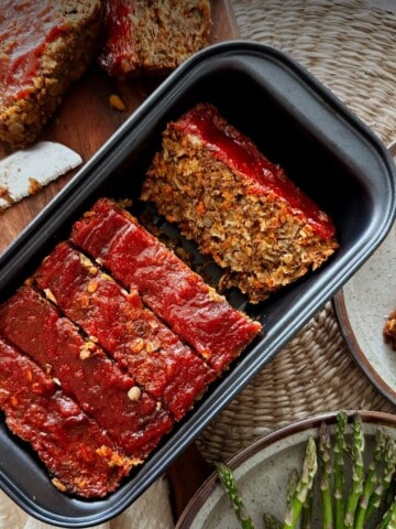 Sliced vegan lentil loaf in a black loaf pan, topped with a glossy ketchup glaze.