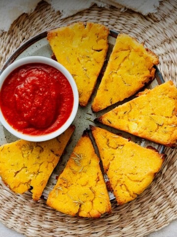 Crispy rosemary polenta wedges arranged on a plate with marinara sauce for dipping.