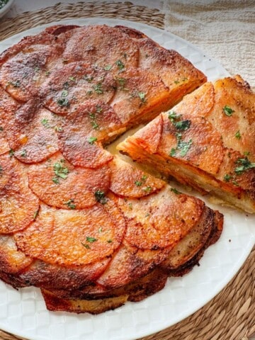 Two-Potato Anna on a white plate with a wedge removed, showing crisp layered sweet potatoes and white potatoes.