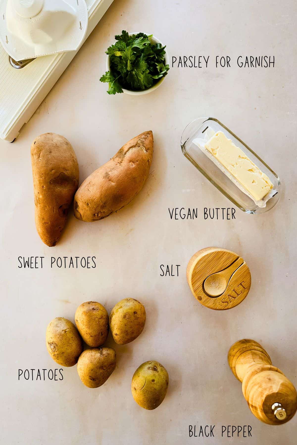 Ingredients for Two-Potato Anna: sweet potatoes, white potatoes, vegan butter, salt, black pepper, and parsley on a light surface.