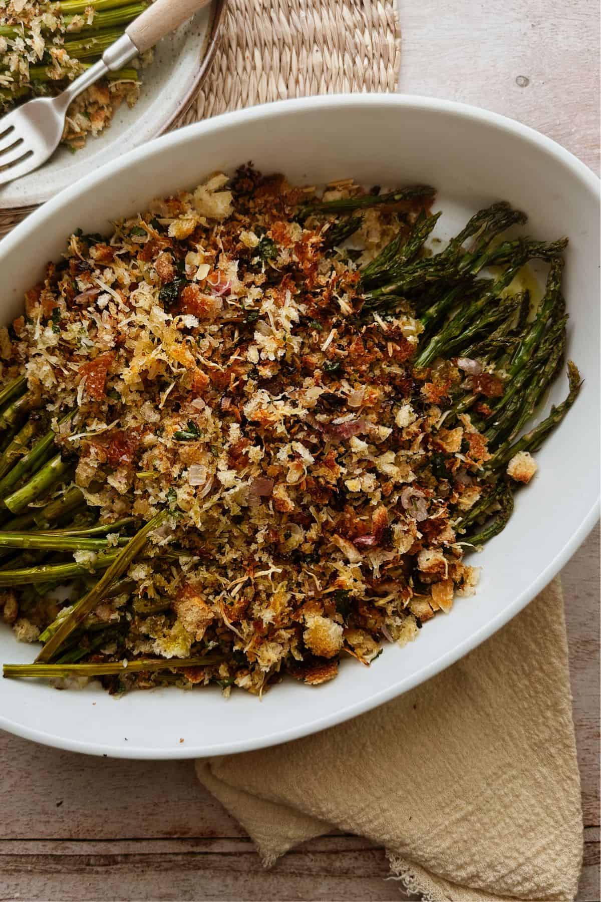 An oval baking dish filled with vegan asparagus gratin, showing tender asparagus spears topped with a crispy, golden breadcrumb mixture.