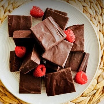 Squares of vegan chocolate fudge on a white plate garnished with fresh raspberries.