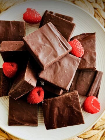 Squares of vegan chocolate fudge on a white plate garnished with fresh raspberries.